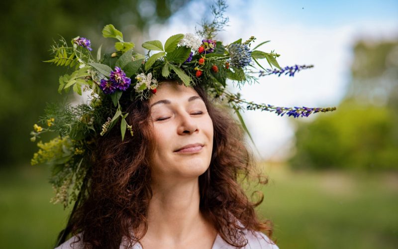 Natural portrait of woman with wildflowers, relaxed in rural summer field. Eco moment of happiness and lightness: woman enjoying summer freedom